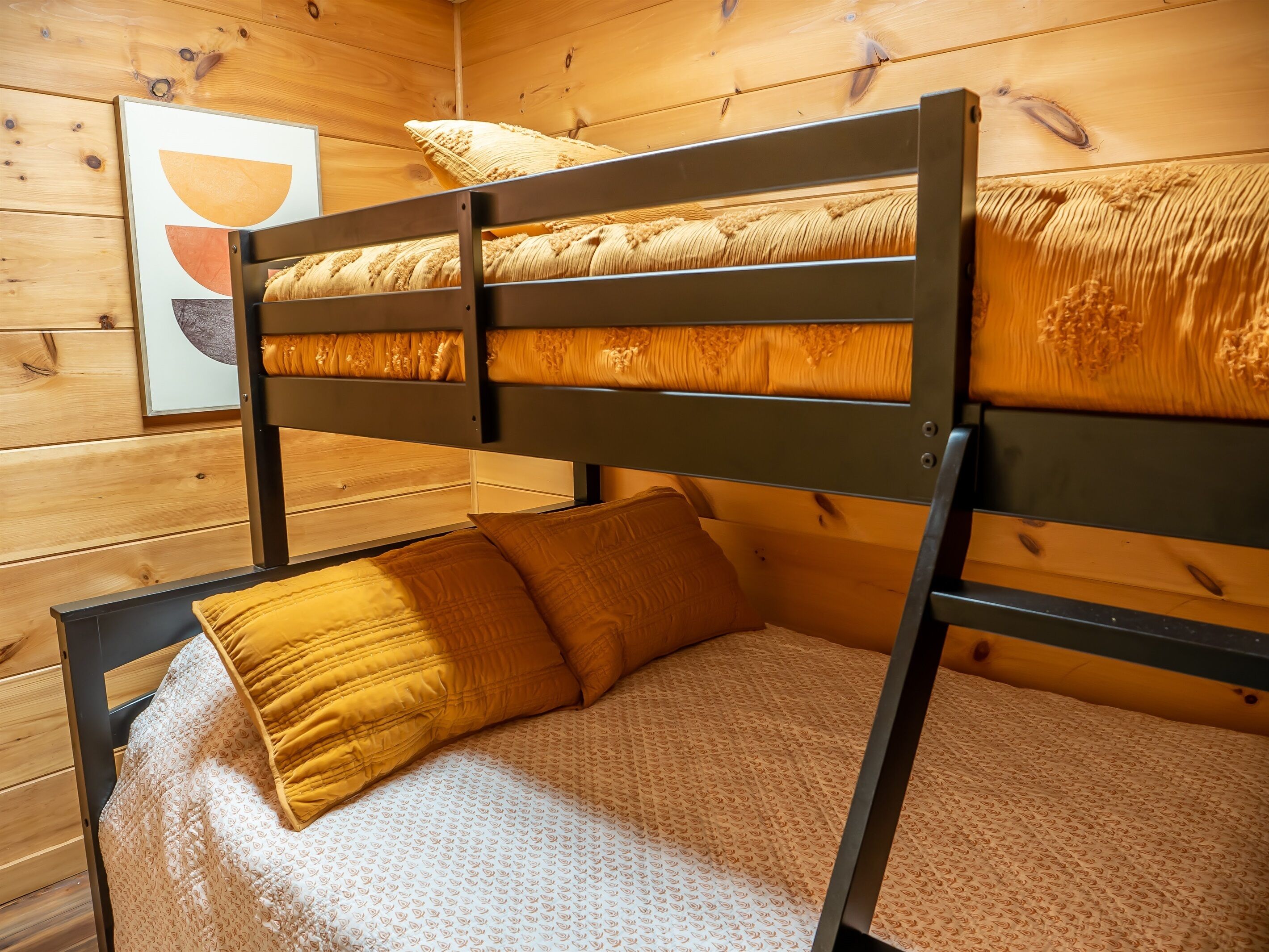 Een stapelbed met een houten hoofdbord, een bedsprei met patroon en een enkel geel kussen.