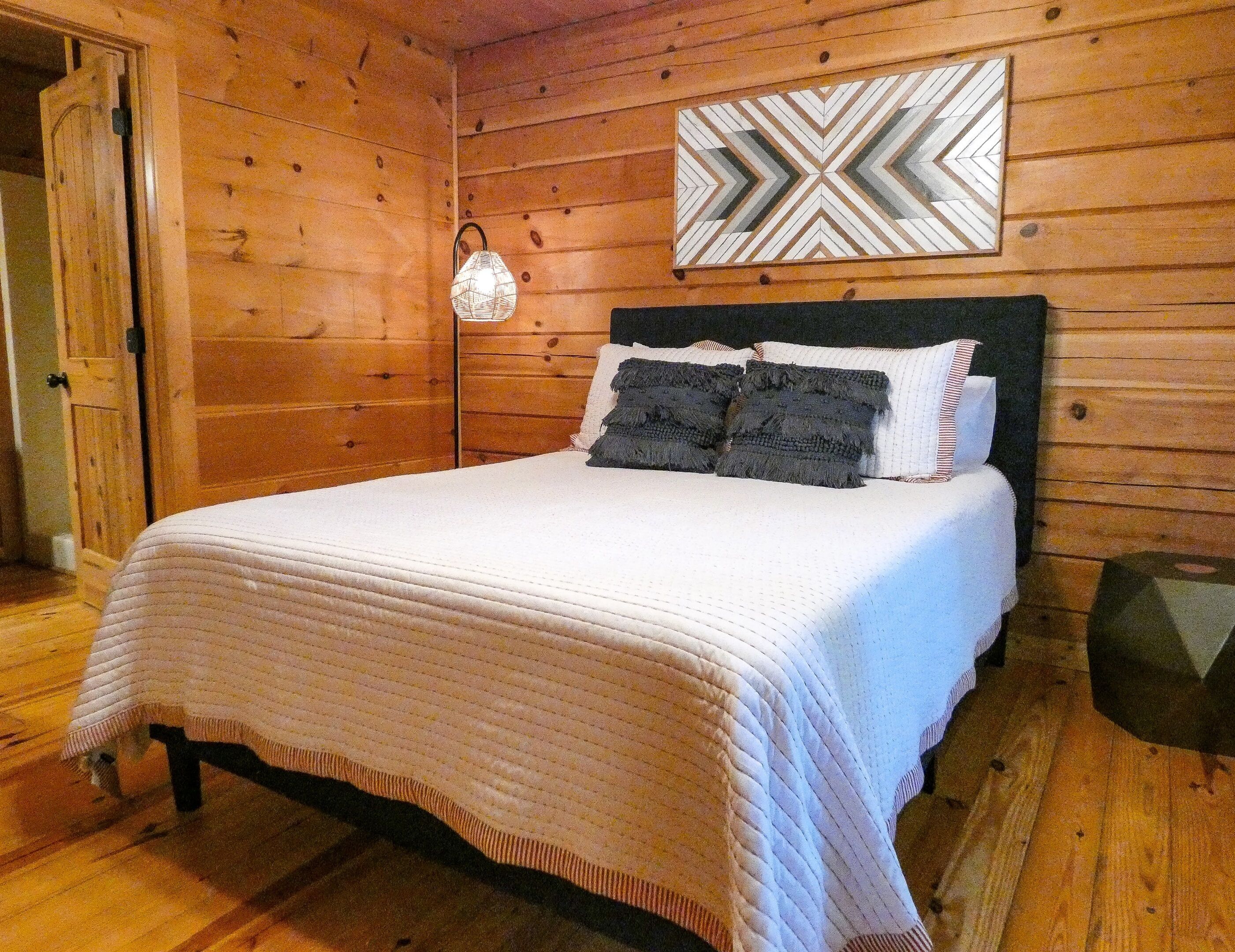 A wooden-paneled room with a bed, a wall-mounted light fixture, and a geometric-patterned wall decoration.