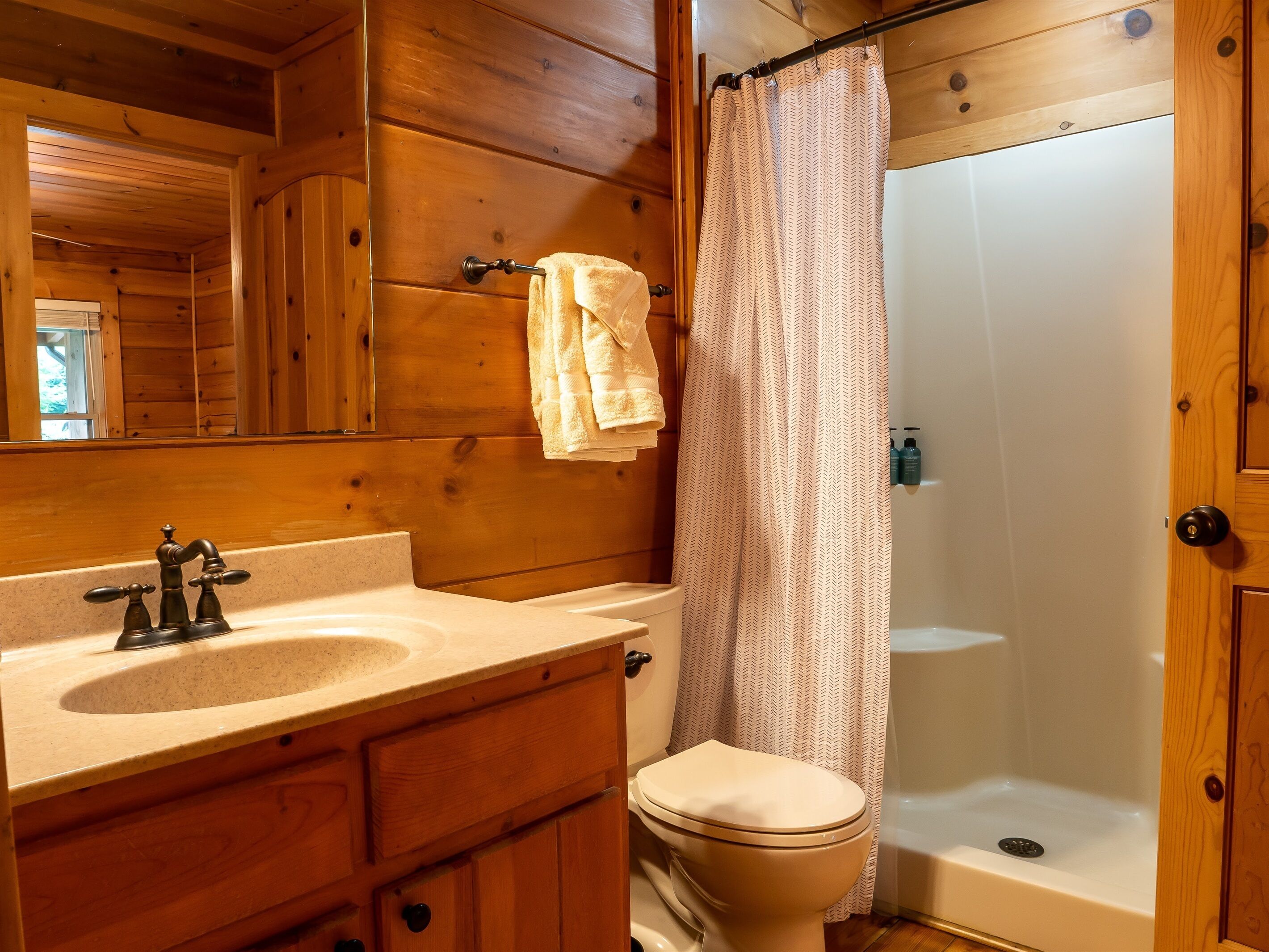 A wooden cabin bathroom with a sink, toilet, and shower.
