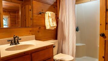 A wooden cabin bathroom with a sink, toilet, and shower.