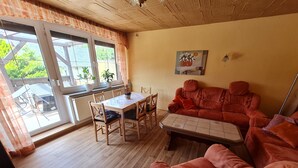 Een gezellige woonkamer met een houten vloer, een eettafel met stoelen, een rode bank en een schilderij aan de muur.