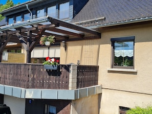 A house with a wooden balcony, a window with a view, and a flower pot. - "Oybinblick" Vacation Apartment in the Zittau Mountains (Oybin)