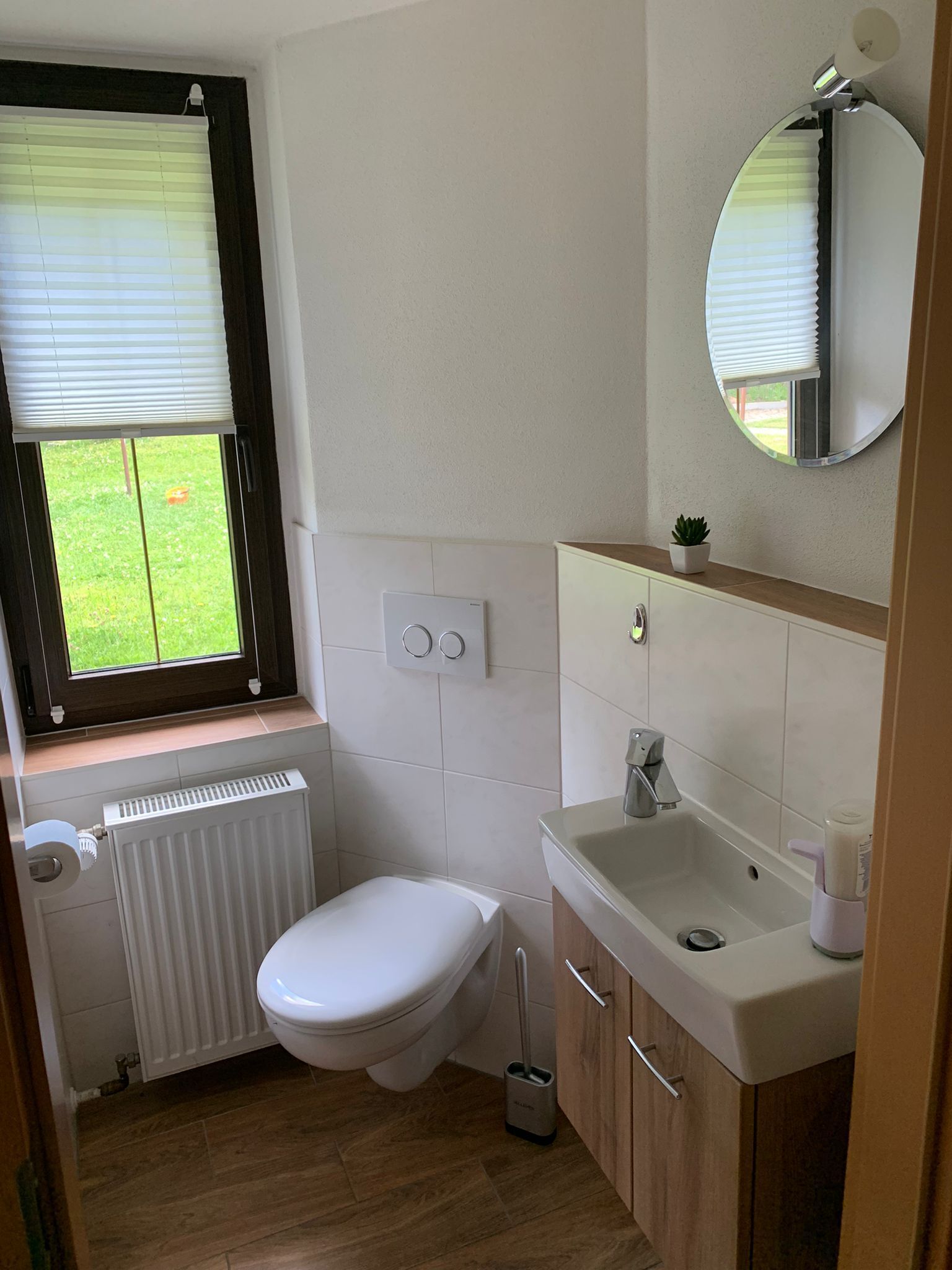 Ein kleines Badezimmer mit Toilette, Waschbecken, Spiegel und Fenster mit Jalousien.
