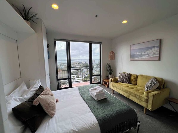 A hotel room with a bed, a sofa, a balcony with a view, and a plant.