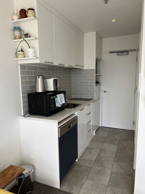 A modern kitchen with white cabinets, a black dishwasher, and a coffee maker on the counter. - Cosy studio with balcony and amazing views! (Auckland)