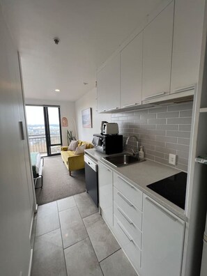 A modern kitchen with white cabinets, a black countertop, and a view to the outside. - Cosy studio with balcony and amazing views! (Auckland)