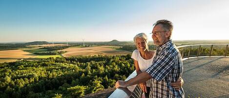 A couple standing on a balcony overlooking a scenic landscape with wind turbines in the distance.
