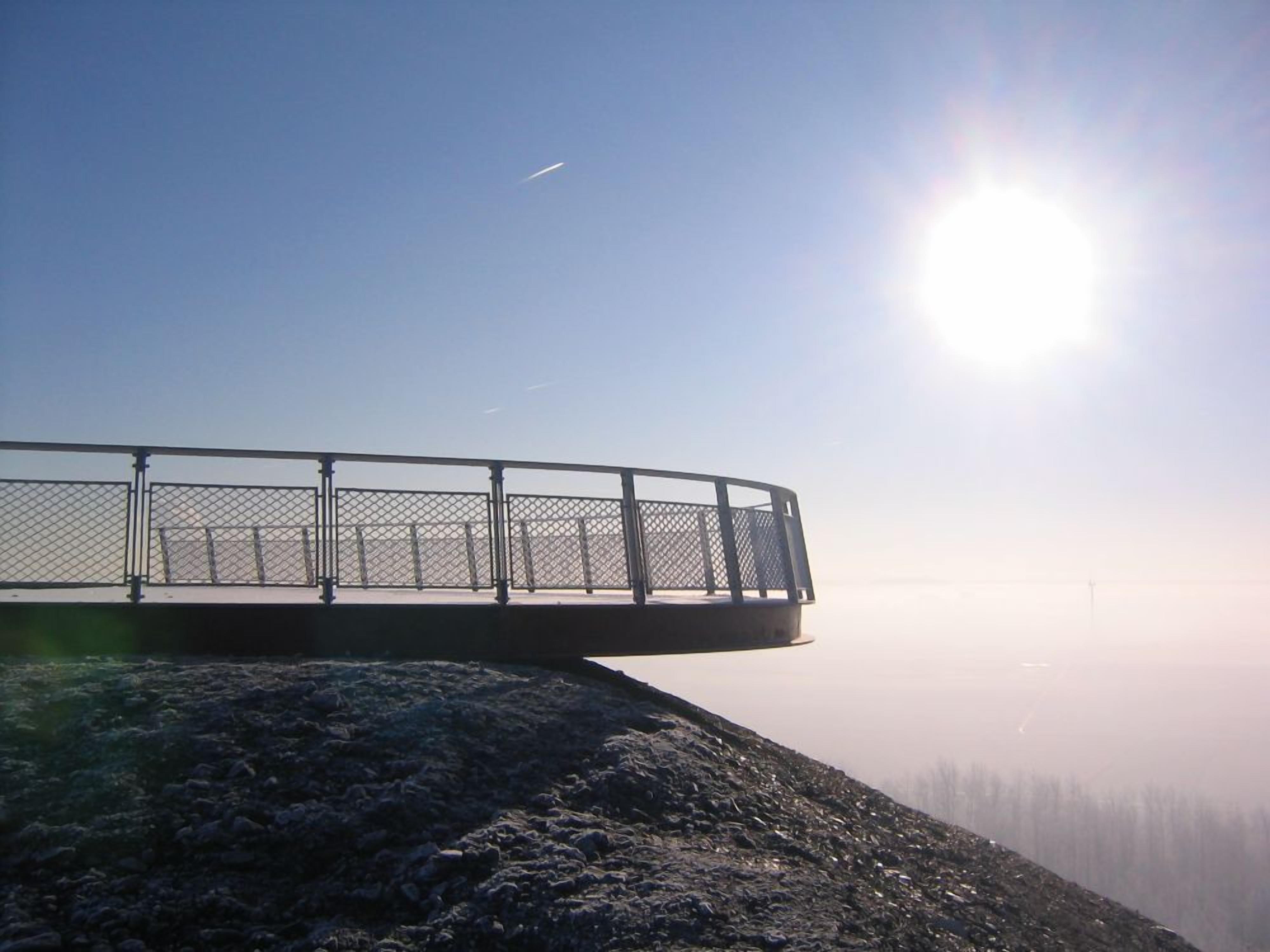 A metal railing overlooking a rocky terrain with a clear sky and the sun shining brightly.