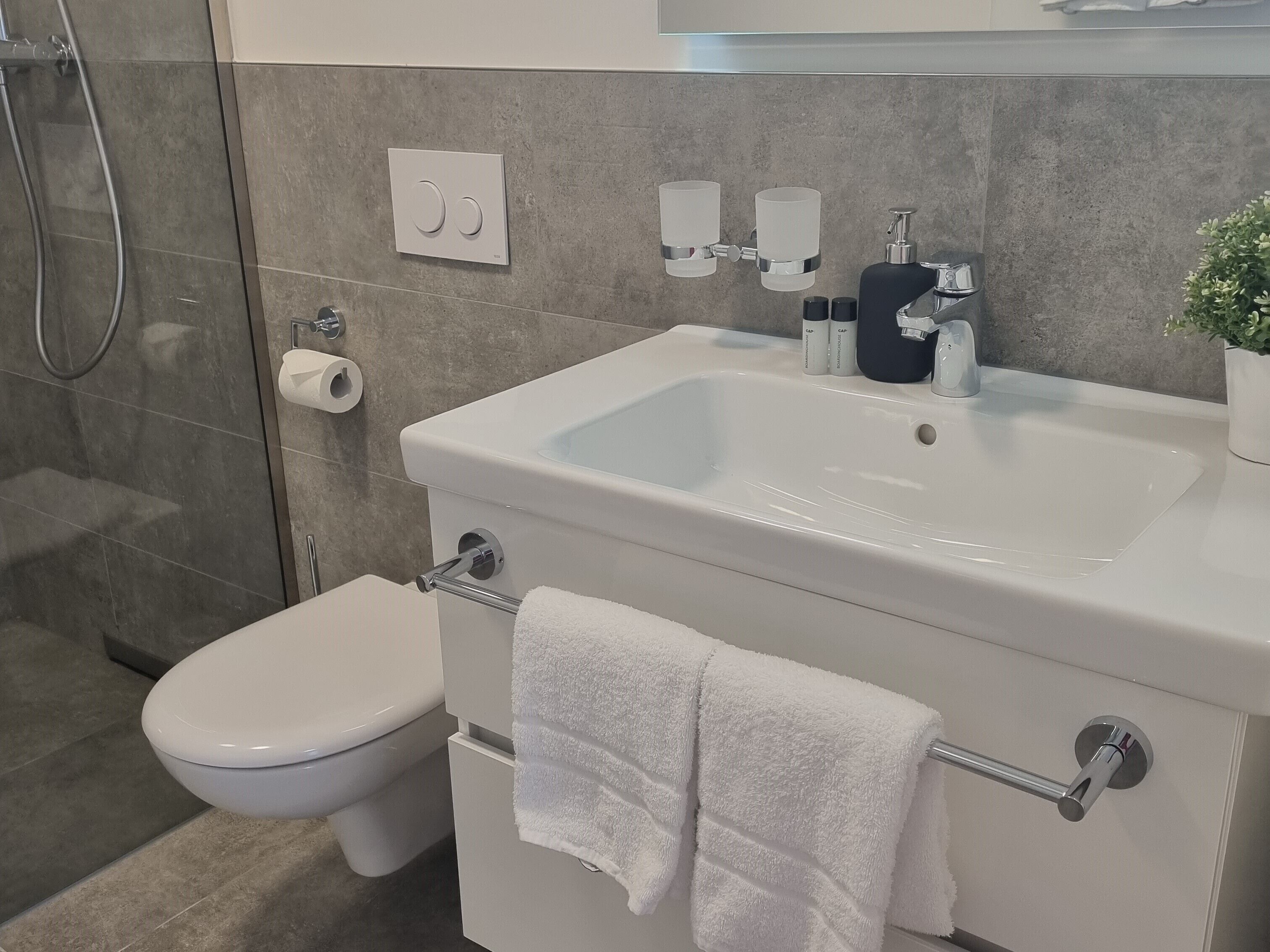 Uma casa de banho moderna com lavatório, sanita e chuveiro brancos.