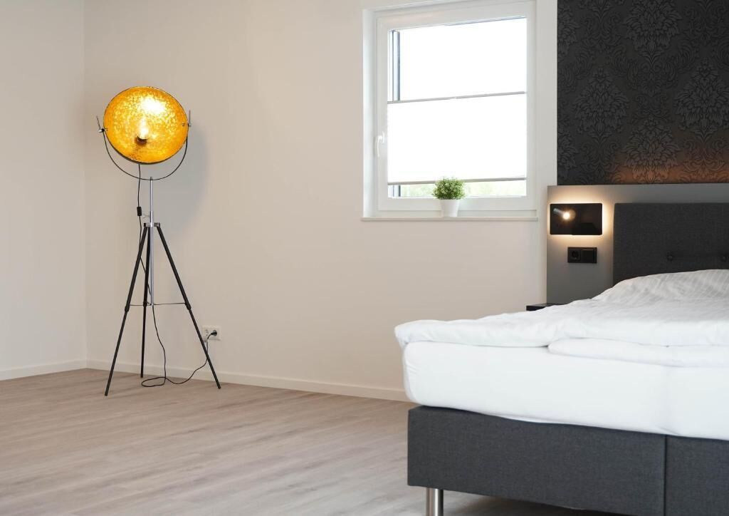 Ein Schlafzimmer mit einem Bett, einer Stehlampe, einem Fenster und einer kleinen Pflanze.
