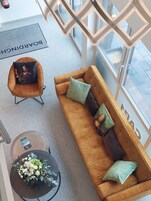 Un interior moderno con un sofá marrón, un sillón con cojín, una mesita con un ramo de flores y un ventanal grande.