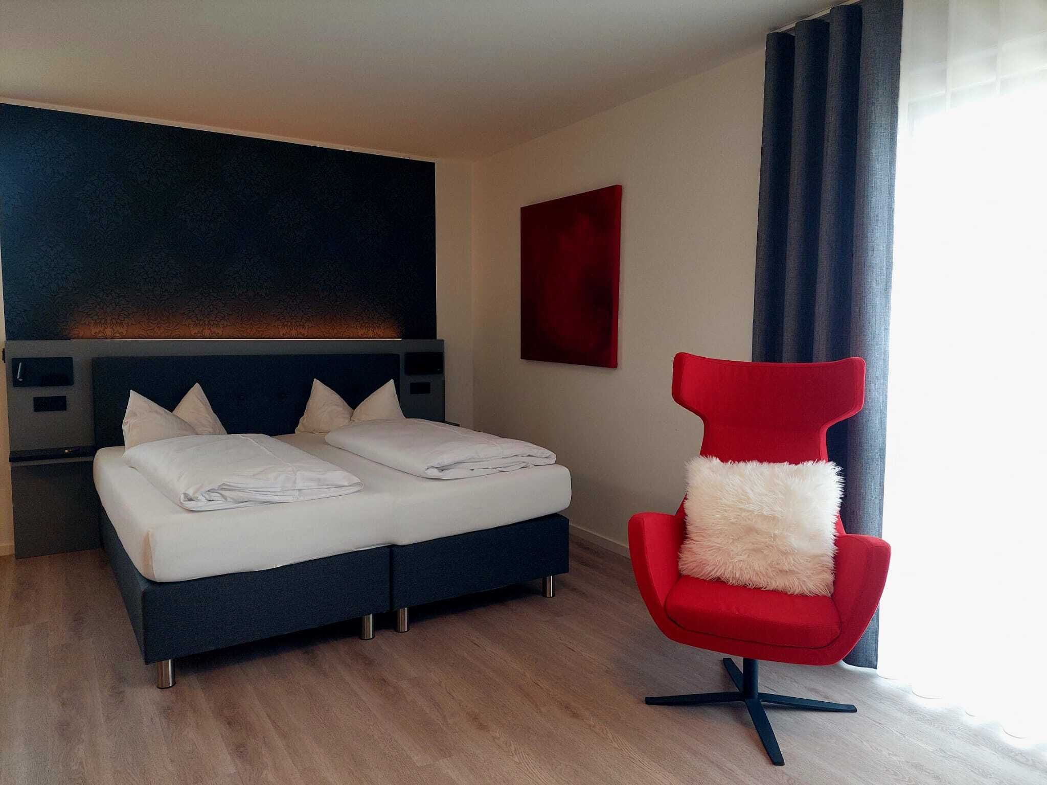 Habitació d'hotel moderna amb un llit, una cadira vermella i un ampli quadre abstracte a la paret.