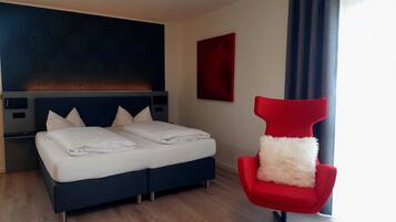 Habitació d'hotel moderna amb un llit, una cadira vermella i un ampli quadre abstracte a la paret.