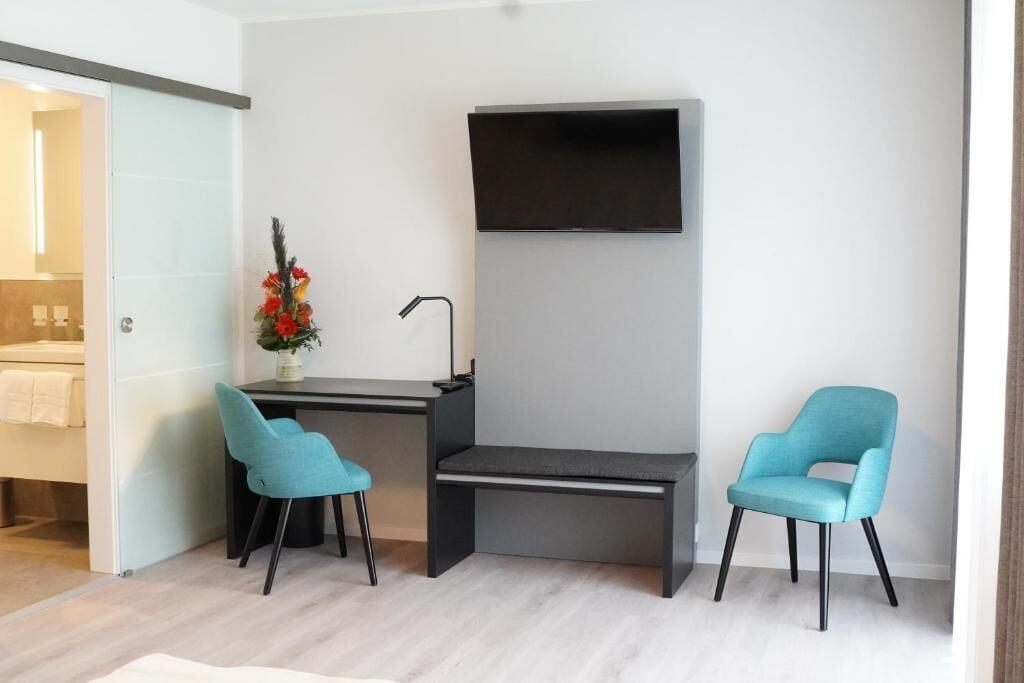 A modern room with a desk, two chairs, a flat-screen TV, and a small plant.