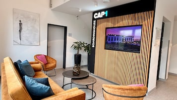 A modern lobby with a seating area, a large screen displaying a cityscape, and a wooden accent wall.
