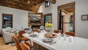 Un comedor con una larga mesa dispuesta para seis personas, una chimenea de piedra y vistas al exterior.