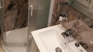 A bathroom with a white sink, a mirror, and a shower area. - Beach Apartment With Garden (Skegness)