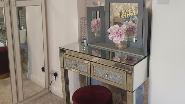 A vanity with a glass top, a mirror, and a vase with flowers. - Beach Apartment With Garden (Skegness)
