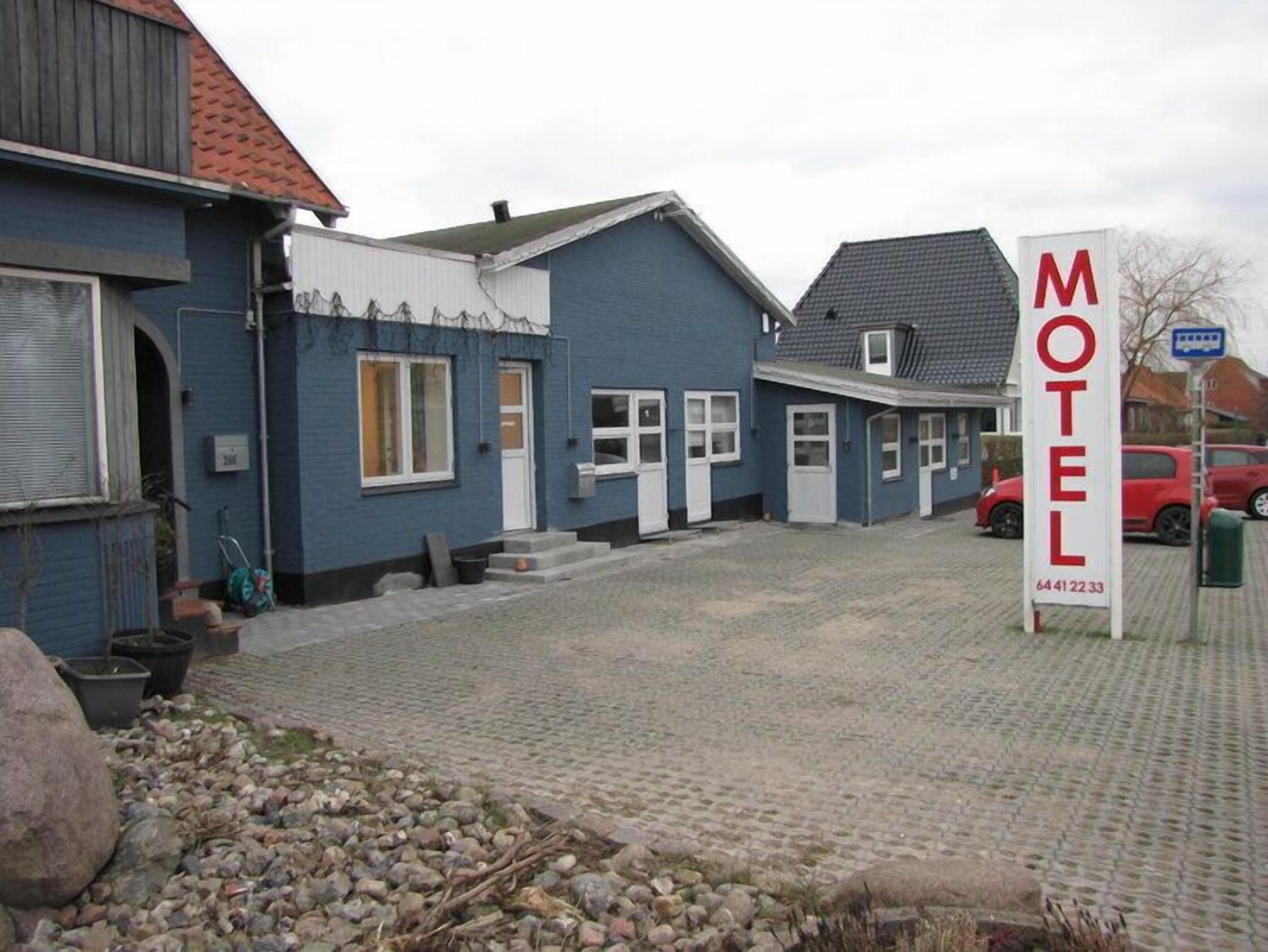 A motel with a signboard, a paved driveway, and a red car parked nearby.