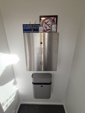 Un dispensador metálico fijado a la pared, con un teclado, un pequeño cubo de basura debajo y un cartel enmarcado arriba.
