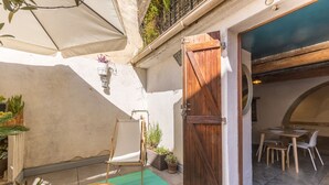 Un patio con una mesa de madera, una silla blanca, una puerta de madera y una zona de comedor con sillas y una mesa.
