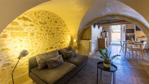 Una sala de estar acogedora con pared de piedra, un sofá, una lámpara y un comedor con sillas y una mesa.