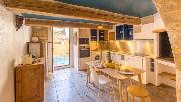 Cocina compacta con vigas de madera, comedor con mesa y sillas, y pared de piedra.