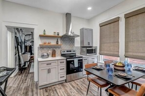 A modern kitchen with white cabinets, a built-in oven, a microwave, and a large window with blinds. - Contemporary Apartment - 5 Min To TIAA Bank Field! (Jacksonville)