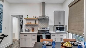 A modern kitchen with grey cabinets, a stove, microwave, and a window with blinds. - Contemporary Apartment - 5 Min To TIAA Bank Field! (Jacksonville)