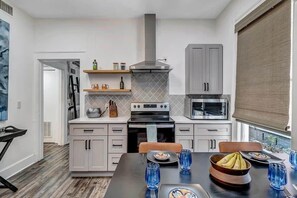 A modern kitchen with grey cabinets, a black stove, and a microwave. There is a dining table with blue glasses and a bowl of bananas. - Contemporary Apartment - 5 Min To TIAA Bank Field! (Jacksonville)
