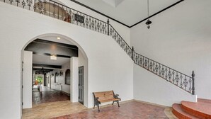 A spacious interior with a brick floor, a wooden bench, and a staircase with ornate metal railings.