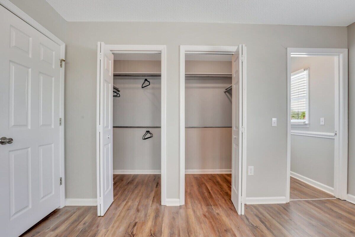 A hallway with two open closets, wooden flooring, and white walls.