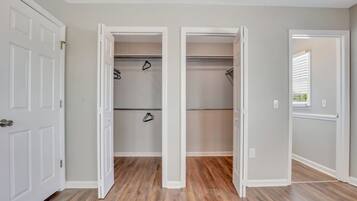 A hallway with two open closets, wooden flooring, and white walls.