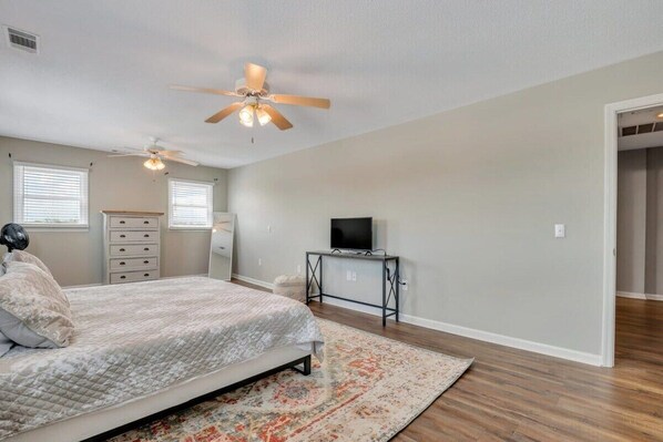 A bedroom with a bed, a ceiling fan, a TV on a stand, and a dresser.