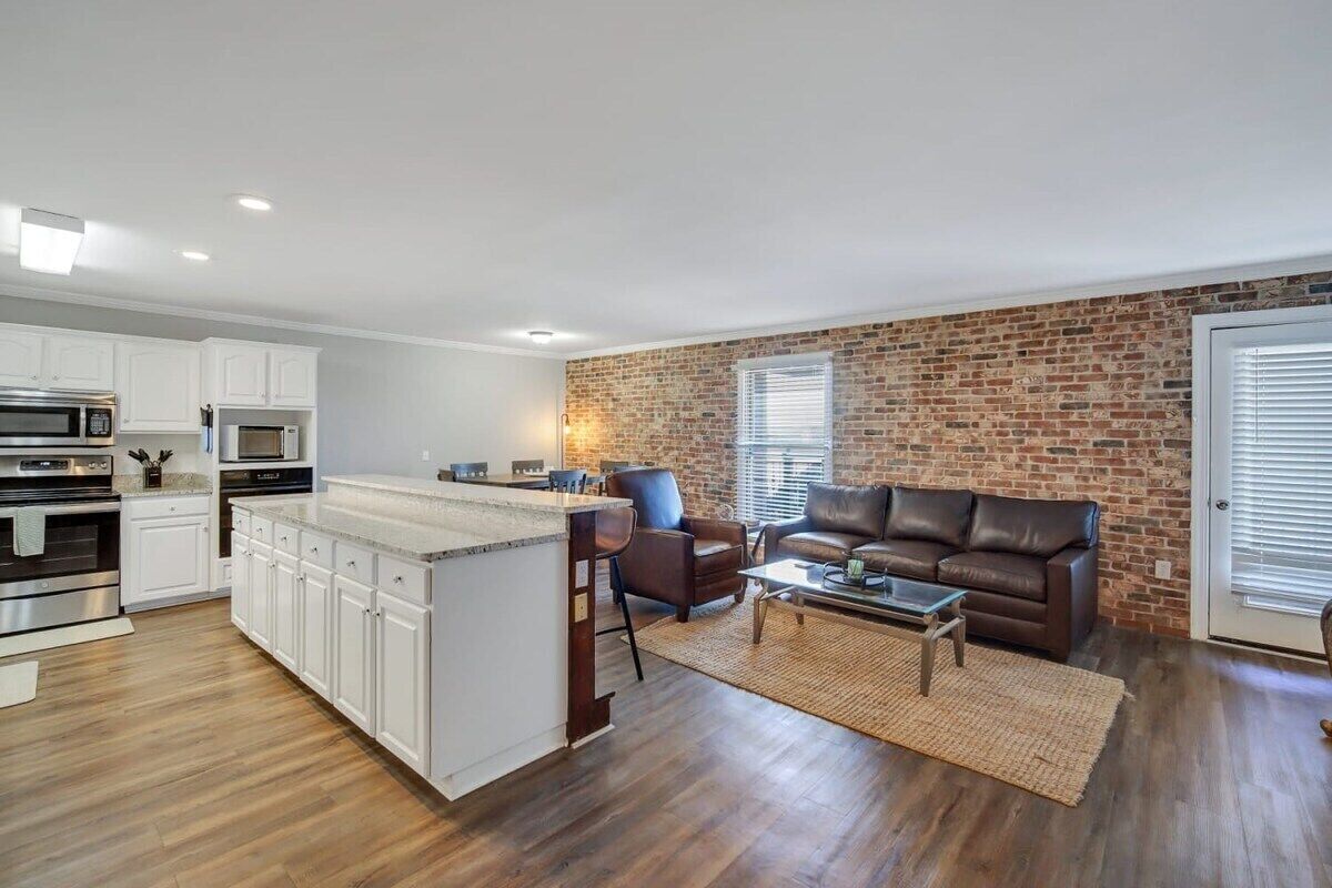 A modern kitchen with white cabinets and stainless steel appliances, a central island, and a brick accent wall.