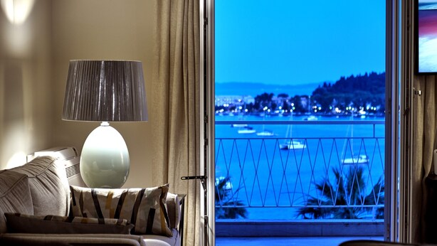 Une chambre d’hôtel avec un balcon donnant sur un plan d’eau, un canapé, une lampe et un téléviseur.