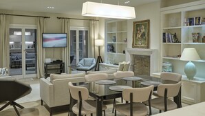 Un salon moderne avec une table basse en verre, des canapés de couleur beige, une cheminée, une bibliothèque et un téléviseur.