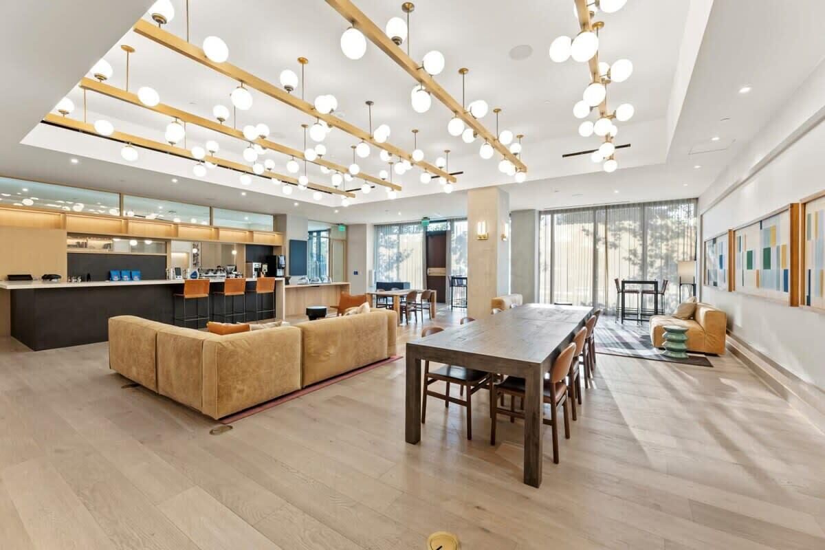 A spacious living area with a wooden dining table, sofas, and a kitchen area with a bar.
