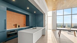 A modern kitchen with a large island, blue cabinetry, and a view of the city through large windows.