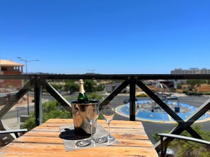 A table with a bottle of champagne and two glasses on a wooden table with a metal railing in the foreground.