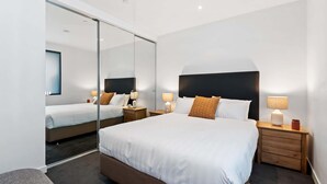Ein modernes Hotelzimmer mit einem großen Bett, Nachttischen, einem Spiegel und einer kleinen Sitzecke.