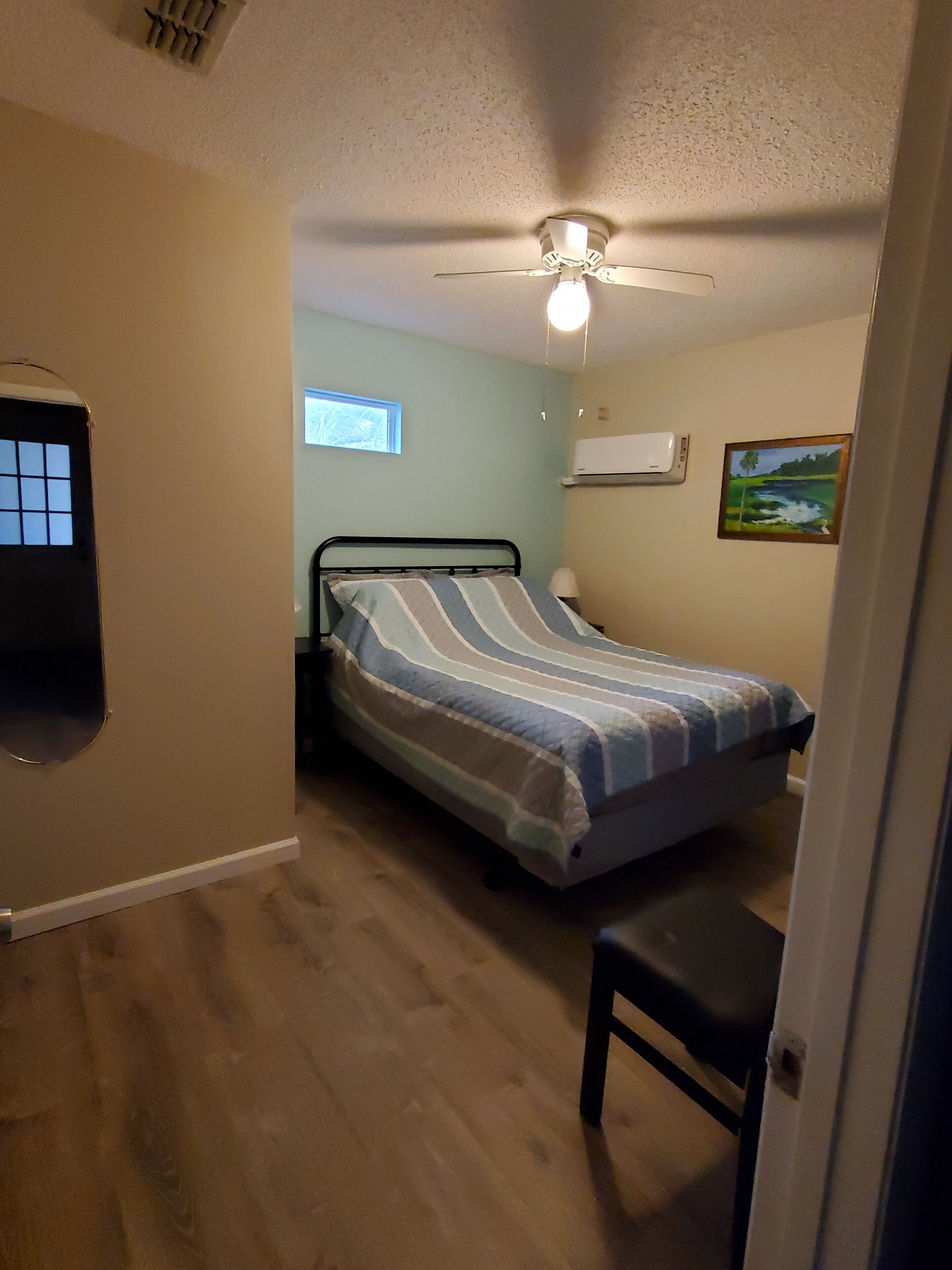 A bedroom with a bed, a ceiling fan, a window, and an air conditioning unit.