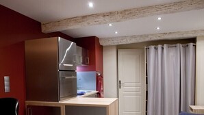 A compact kitchen with a built-in refrigerator, a small countertop, and a dining area with a blue sofa. - Very Nice Studio Ideal For 2 Near The Halles (Avignon)