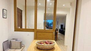 A modern kitchen with a wooden table, a fruit basket, and a stainless steel appliance.