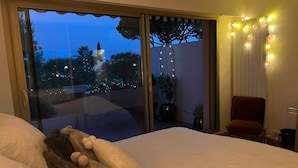 A bedroom with a large bed, a view of the outdoors, and a chair by the window.
