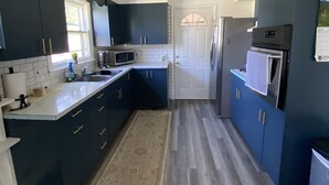 A modern kitchen with dark blue cabinets, a white countertop, a stainless steel refrigerator, and a built-in microwave. - Entire Home with Lakeview (L'Anse)