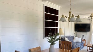 A dining area with a wooden table and chairs, a vase with a plant, and a large window with shelves. - Entire Home with Lakeview (L'Anse)