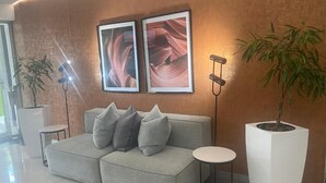 A modern living room with a grey sofa, two framed pictures on the wall, a small round table, and two potted plants. - Central Rosebank Unit (Johannesburg)