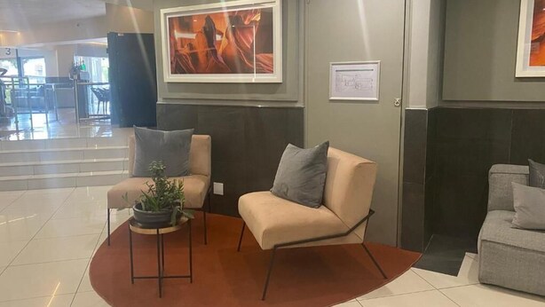 A modern lobby with a beige sofa, a small table with a plant, and a framed picture on the wall. - Central Rosebank Unit (Johannesburg)