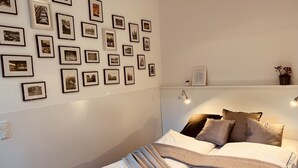 A bedroom with a neatly made bed, a wall adorned with numerous framed photographs, and a small shelf with a potted plant. - Charming rear building near the old town (Osnabrück)